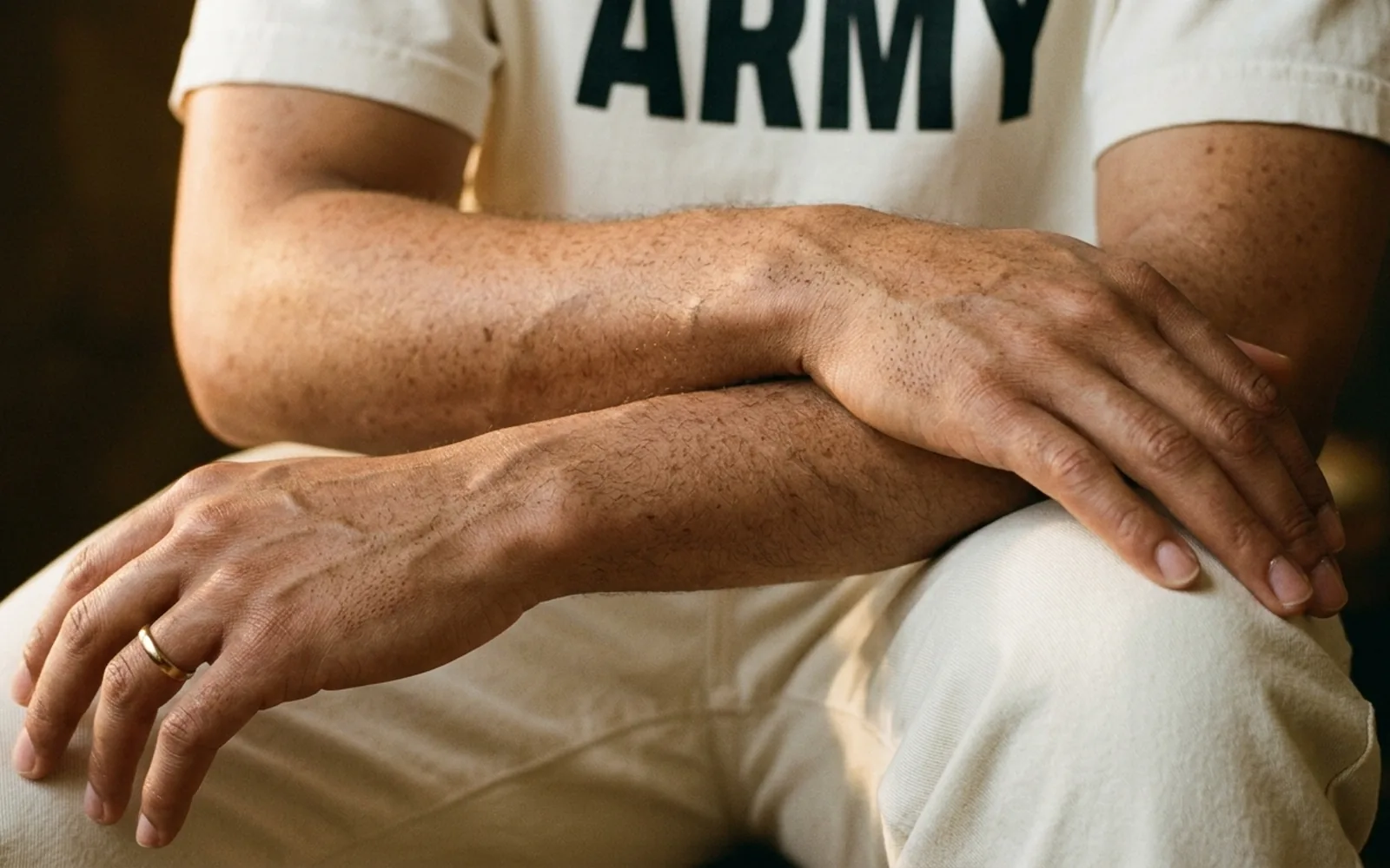 Freckled forearms and hands resting on a knee in warm side light, an Ivory Loud and Proud tee above