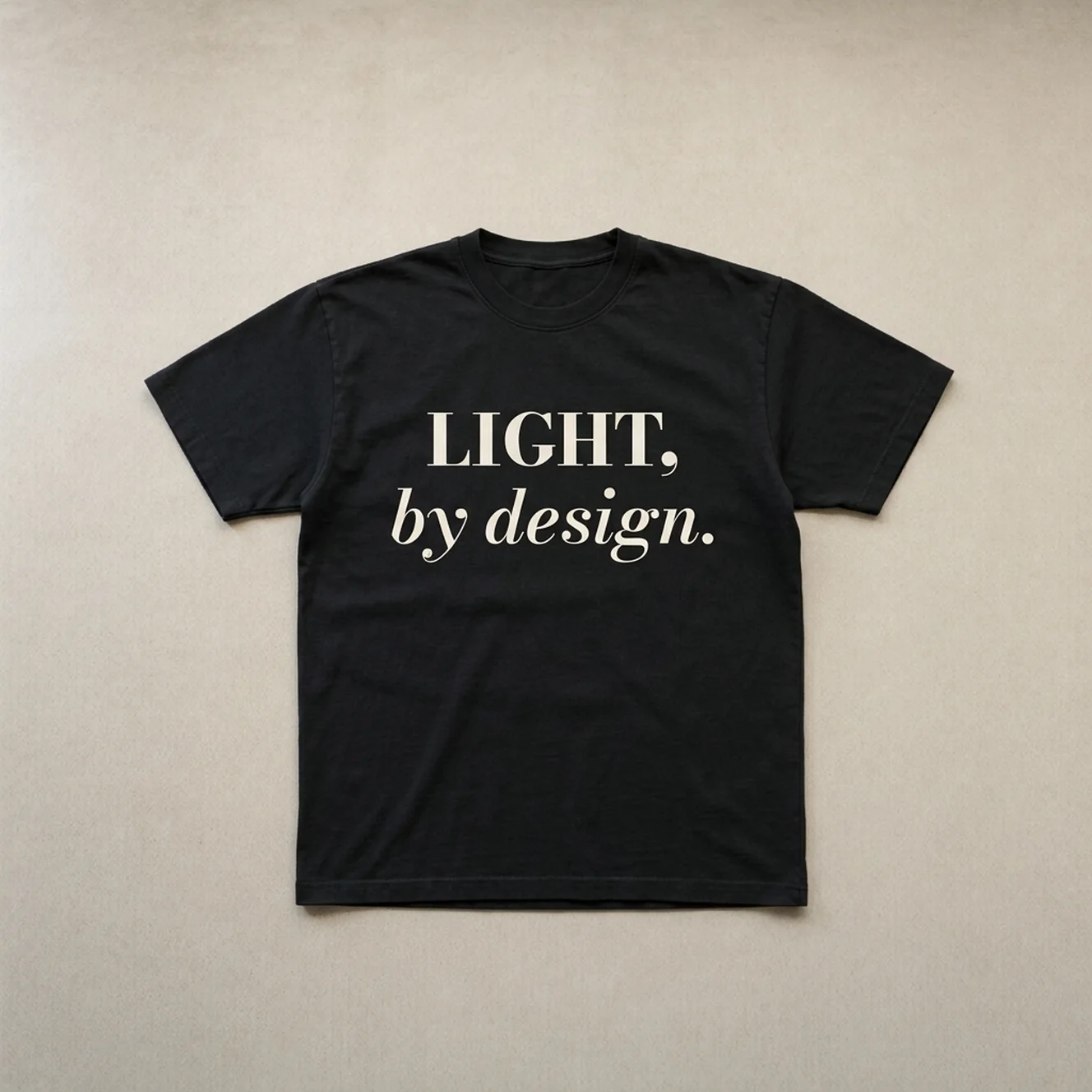 Light By Design tee in Black laid flat on warm concrete
