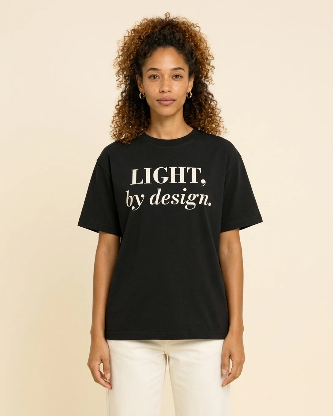 Model wearing the Light By Design tee in Black, reading LIGHT, by design.