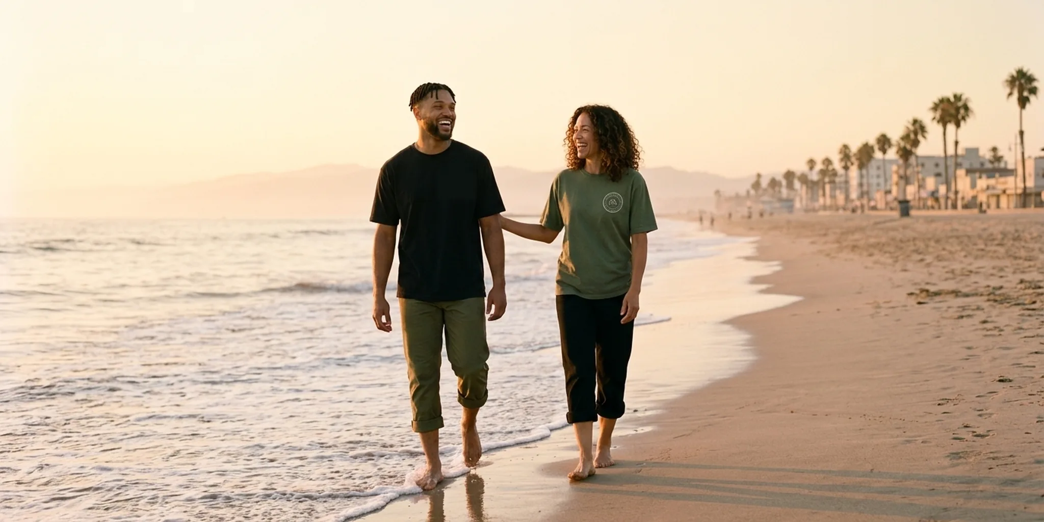 Dre and Simone walking barefoot at the Venice Beach waterline at golden hour, laughing